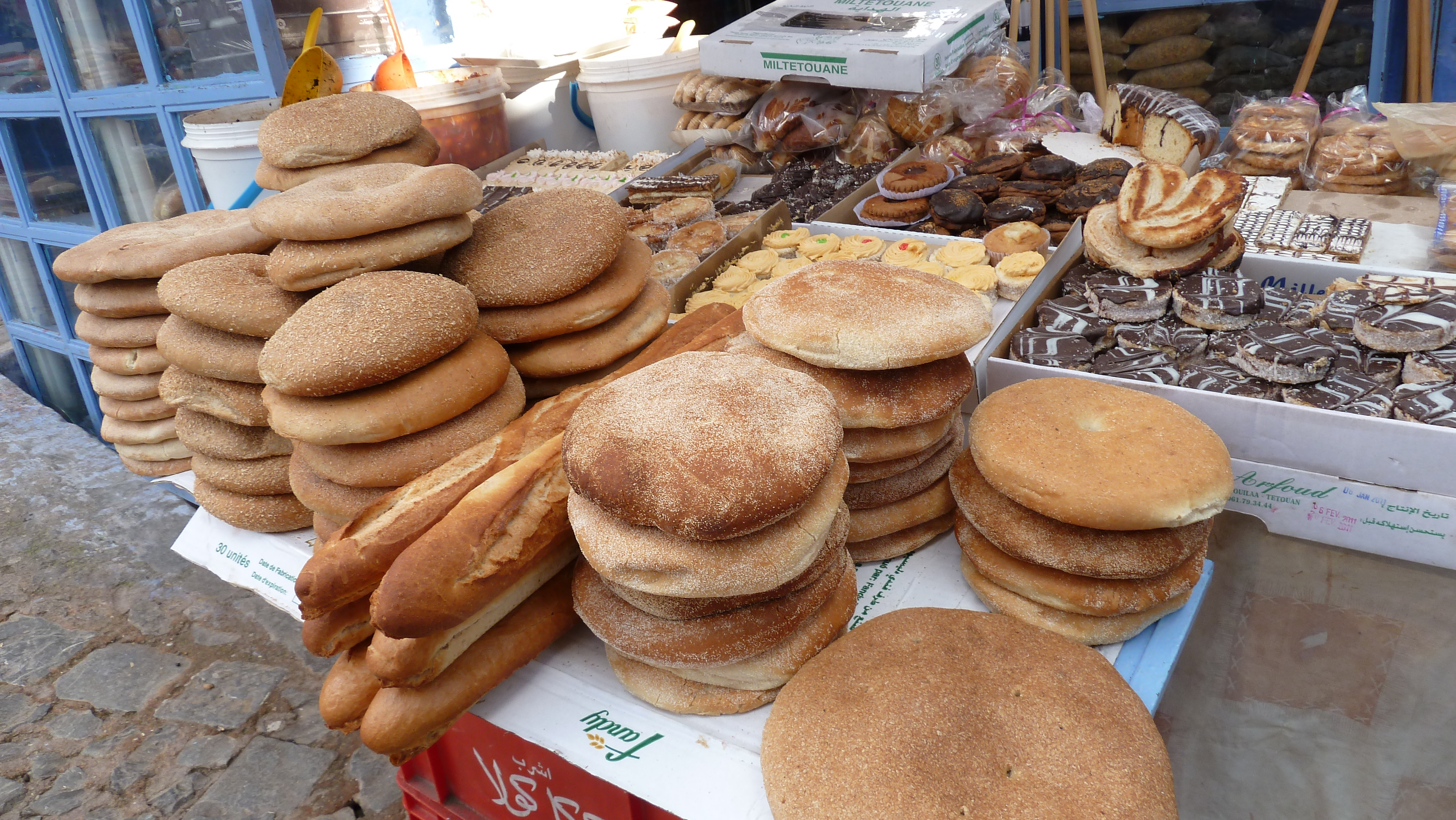Bakery stall in Chefchaouen's medina featuring stacks of fresh breads and pastries against blue walls
